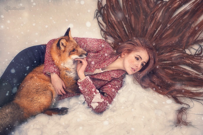 Woman with long red hair and fox in the snow
