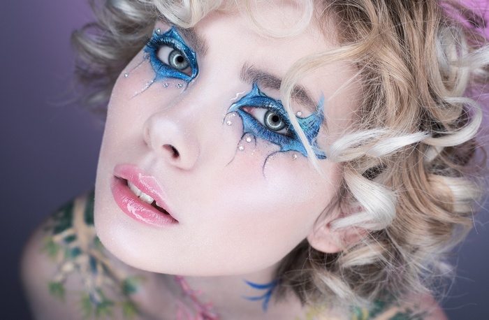 Woman with blue fantasy makeup and blonde curly hair