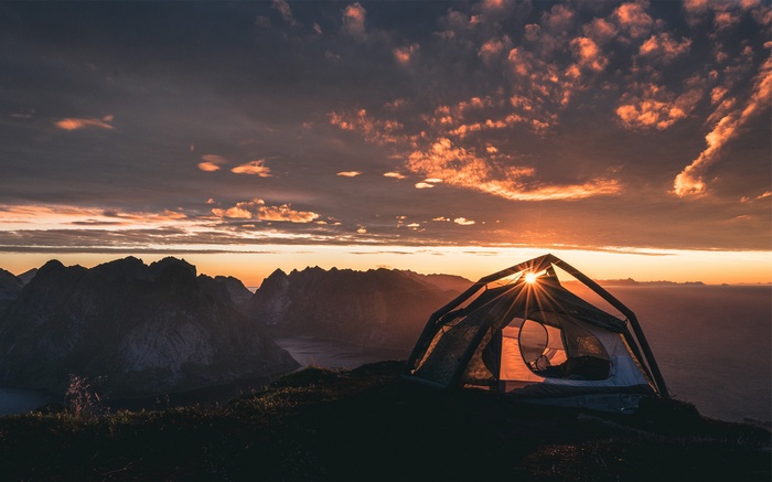 Tent on mountain peak at sunset with sun rays