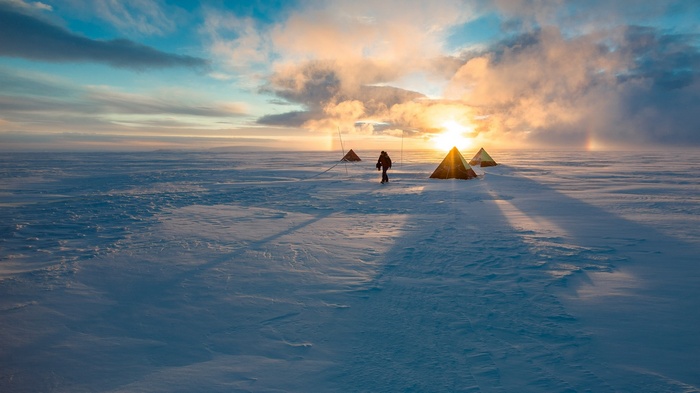 Person walking between tents in a snowy landscape at sunset
