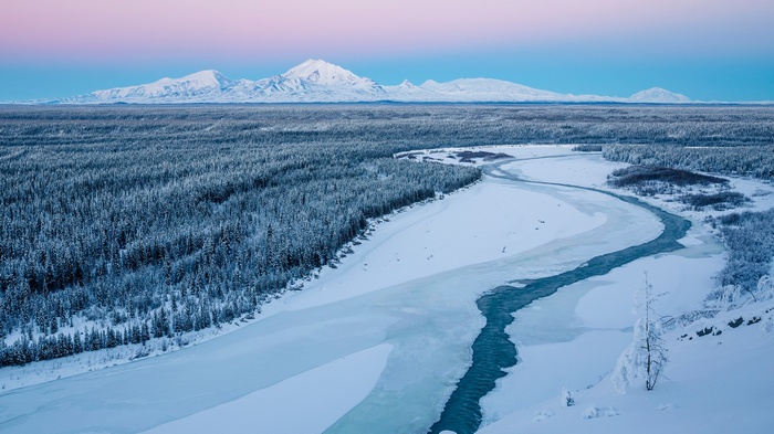 Snowy forest and river with mountains in the background