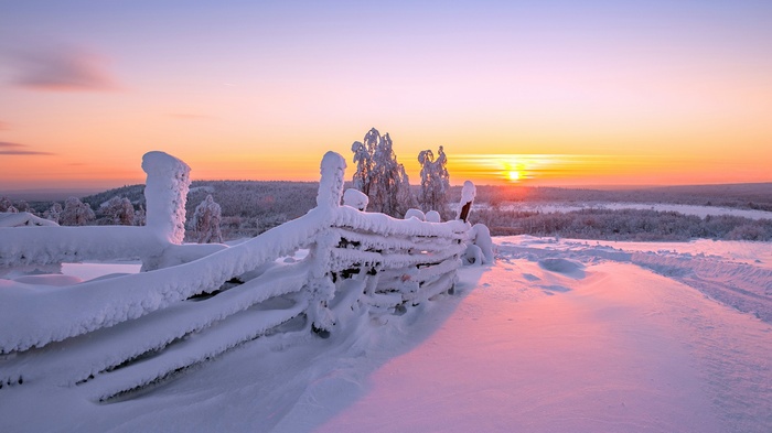 Snow-covered fence at sunrise in winter landscape