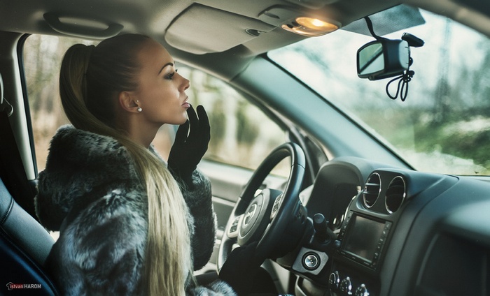 Woman in fur coat applying lipstick in car