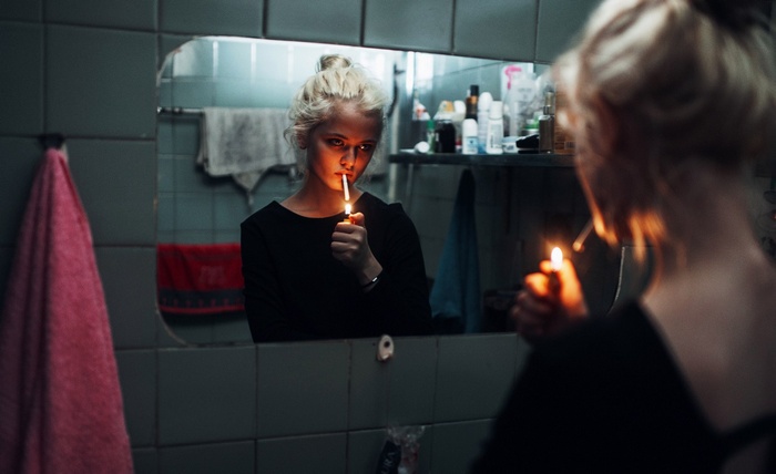 Woman lighting cigarette in bathroom mirror