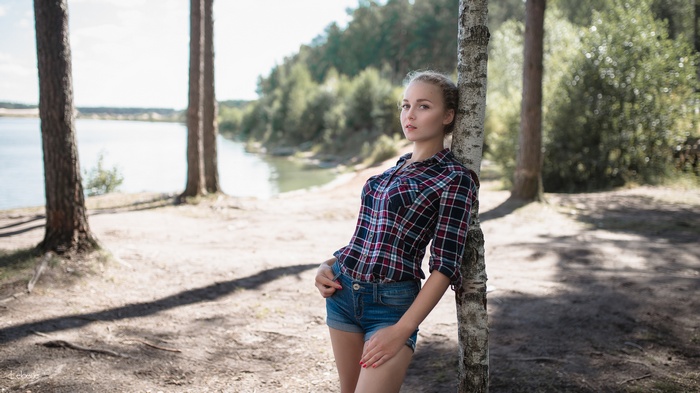 Woman in plaid shirt and jean shorts leaning on tree
