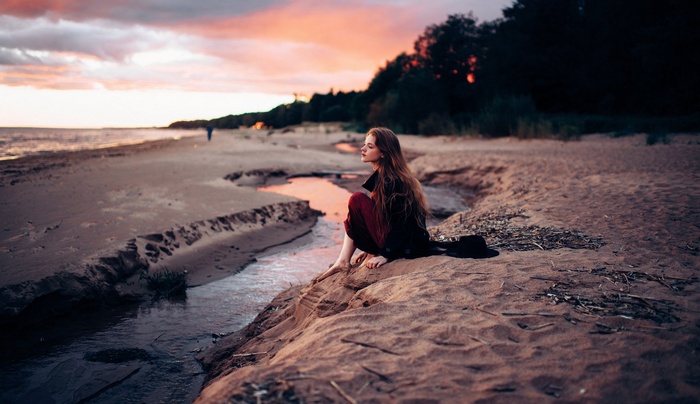 Woman sitting on a sandy beach at sunset