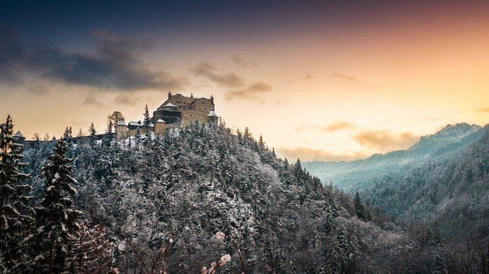 Castle on a snow-covered mountain with forest and sunset sky