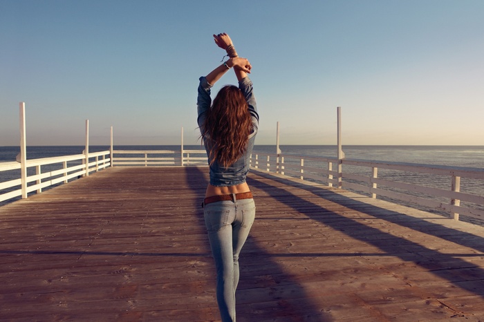 Woman in jeans on a pier with arms raised