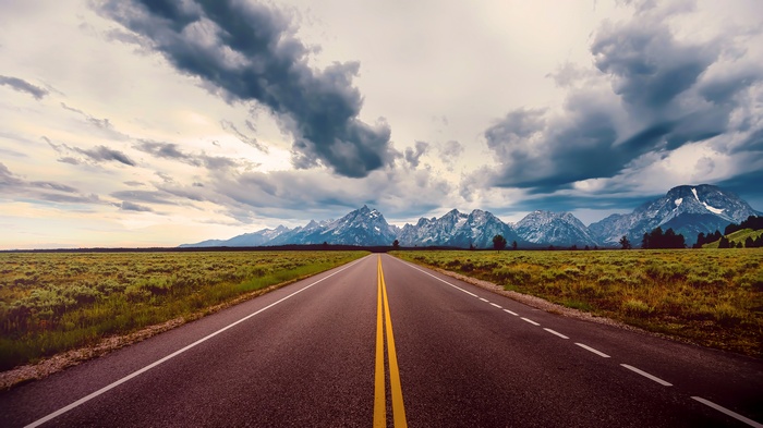 Road leading to snow-capped mountains under cloudy sky