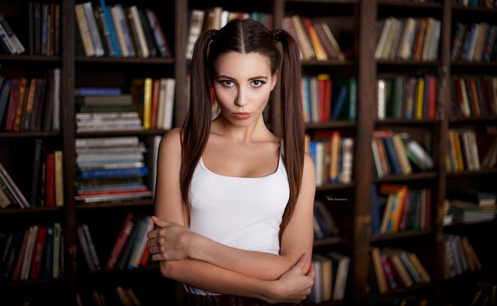 Woman with pigtails in white top in front of bookshelves