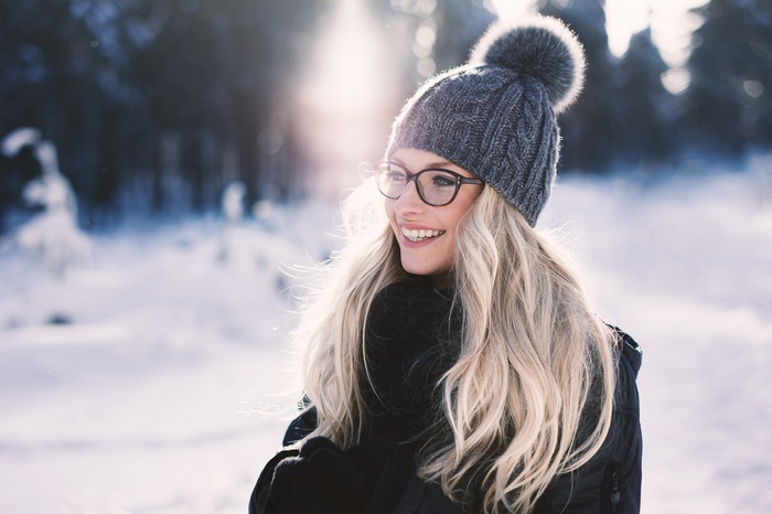 Woman in winter hat and glasses smiling in snow