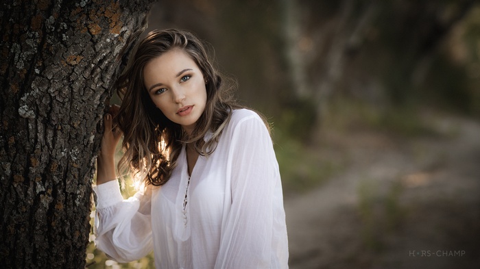 Woman in white shirt leaning against a tree