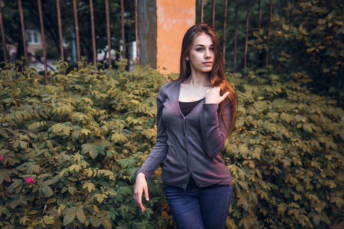 Woman in cardigan and denim standing near bushes