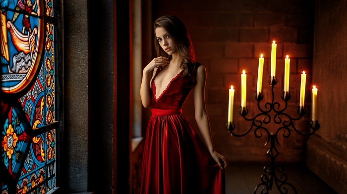 Woman in red dress by stained glass and candles