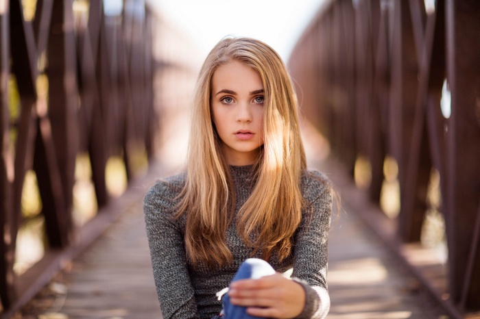 Blonde girl with blue eyes sitting on a bridge