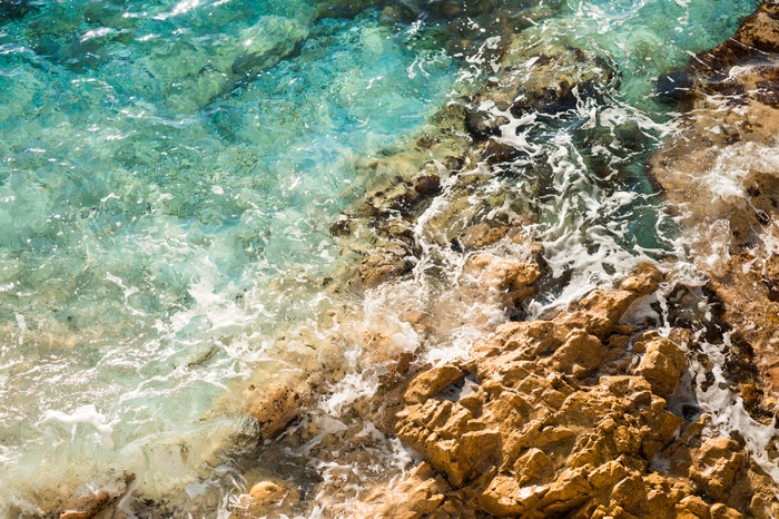 Clear blue sea waves crashing on rocky shore