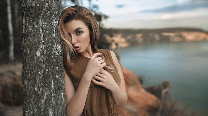 Woman leaning against a tree by a lake