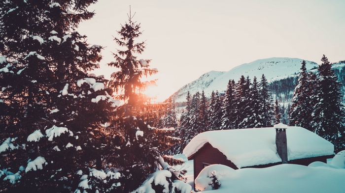 Snowy cabin in Norway with pine trees and mountains at sunrise