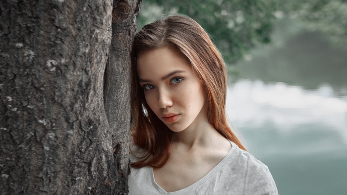 Woman with blue eyes leaning against a tree