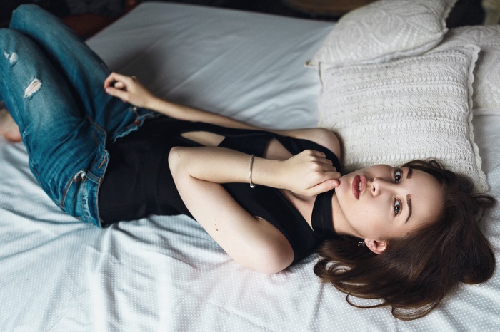 Woman in torn jeans and black bodysuit lying on bed