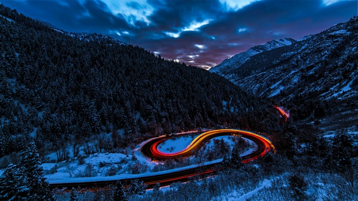 Long exposure of a winding road through a snowy mountain forest at dusk
