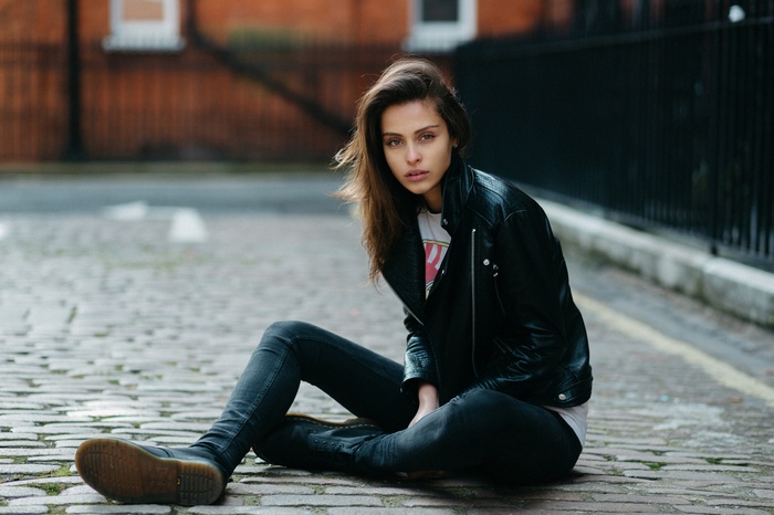 Woman in leather jacket sitting on cobblestone street