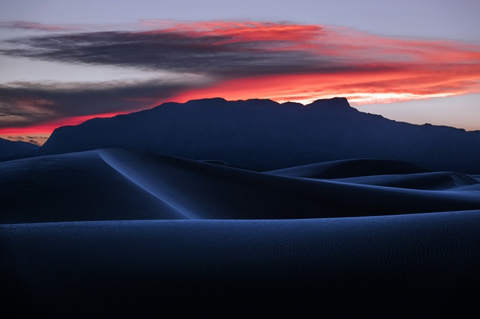 Dark sand dunes at sunset with mountain silhouette