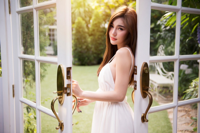 Asian woman in white dress standing by open doors