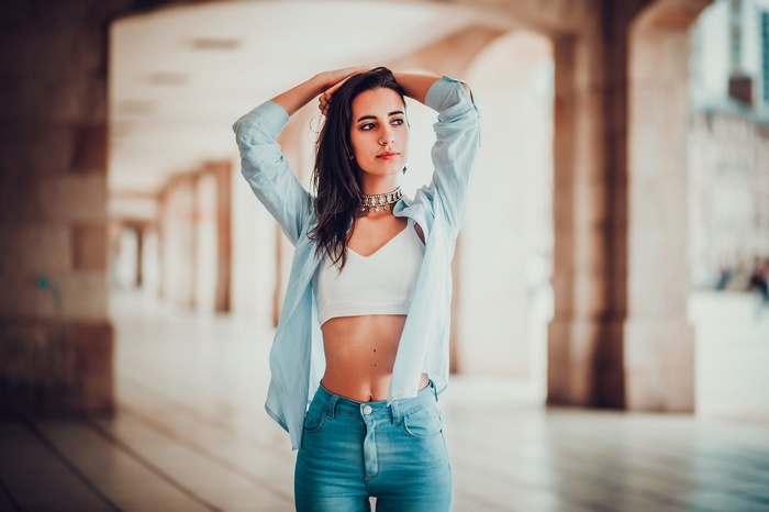 Woman in blue shirt and jeans with hands on head