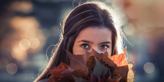 Woman holding autumn leaves in front of her face