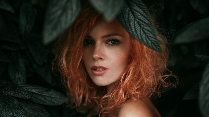 Portrait of a redhead woman among dark leaves