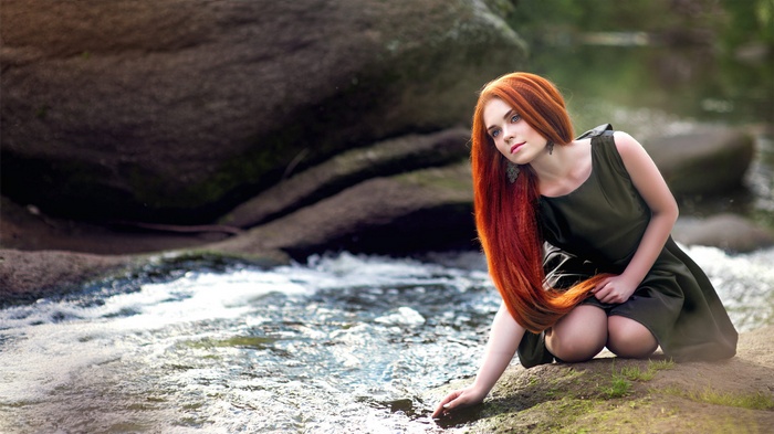 Redhead woman kneeling by a stream
