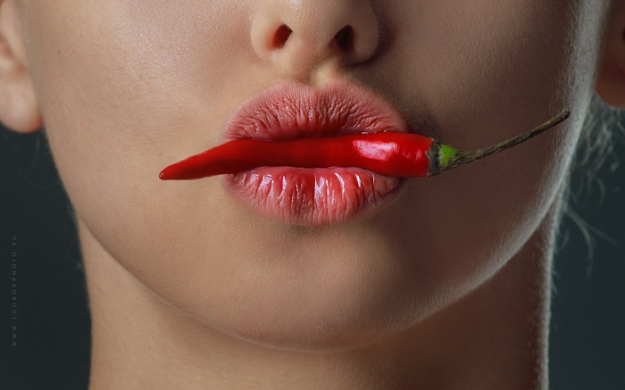 Woman with red chili pepper on lips