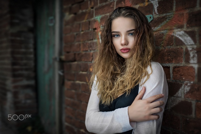 Woman with blue eyes and curly hair leaning against brick wall