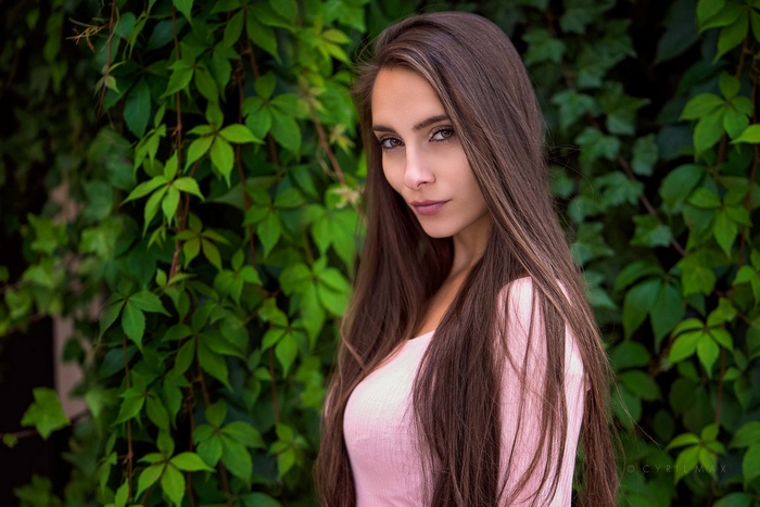 Pavlina with long brown hair in front of green leaves