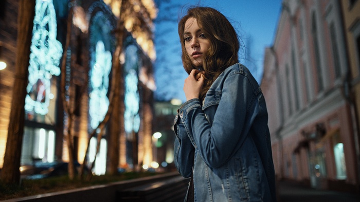 Woman in denim jacket at night with city lights