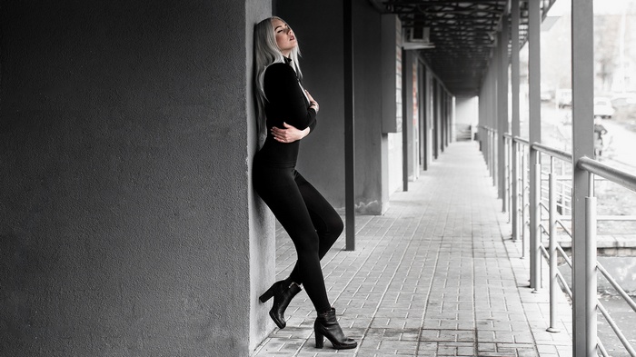 Woman with white hair in black clothing leaning against a wall
