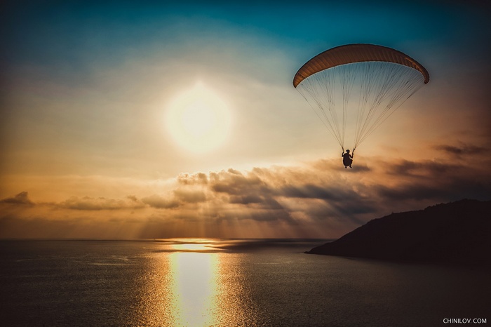 Paraglider flying over the ocean at sunset