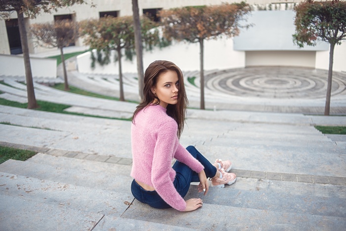 Woman in pink sweater sitting on stairs outdoors