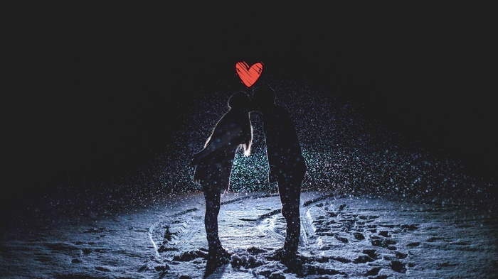 Couple kissing in the snow at night with a heart