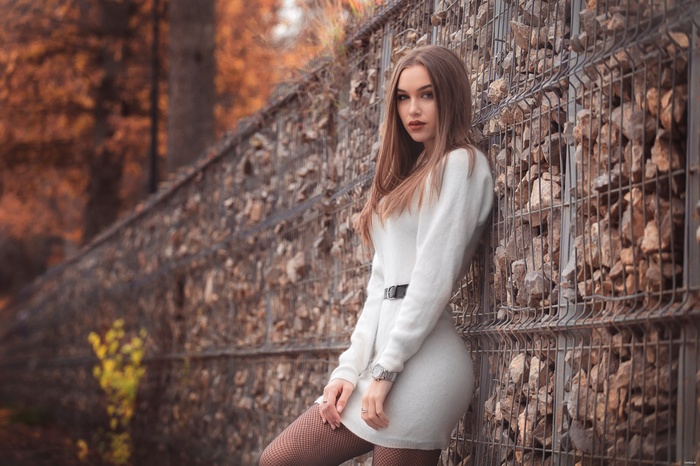 Woman in white dress leaning against a stone wall