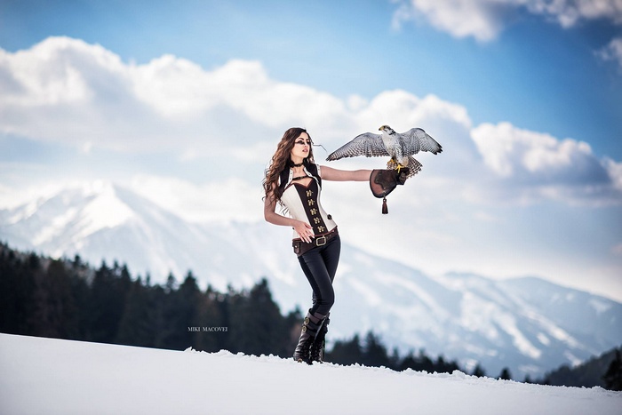 Woman in corset with falcon in snowy mountains