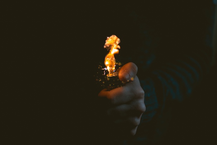 Hand holding a lit lighter with flames