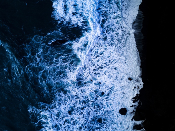 Aerial view of ocean waves crashing on a dark shore