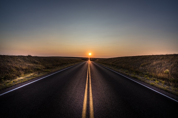 Asphalt road leading to the sunset over a prairie landscape