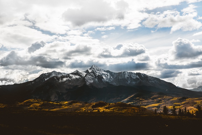 Snowy mountain range with yellow trees and clouds
