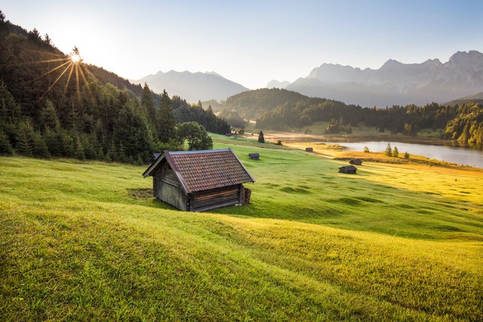 Wooden cabin in a green meadow with mountains and lake