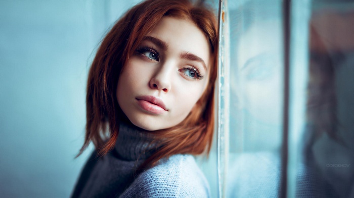 Redhead woman with blue eyes looking out a window