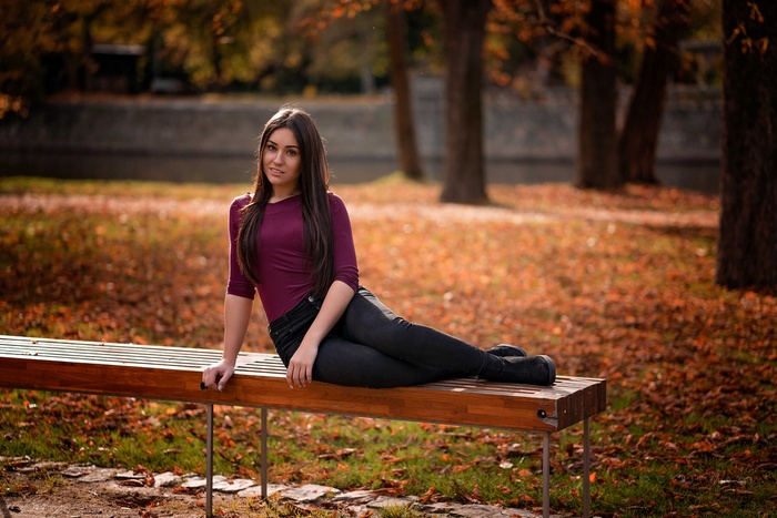 Woman in burgundy top and black jeans sitting on a park bench