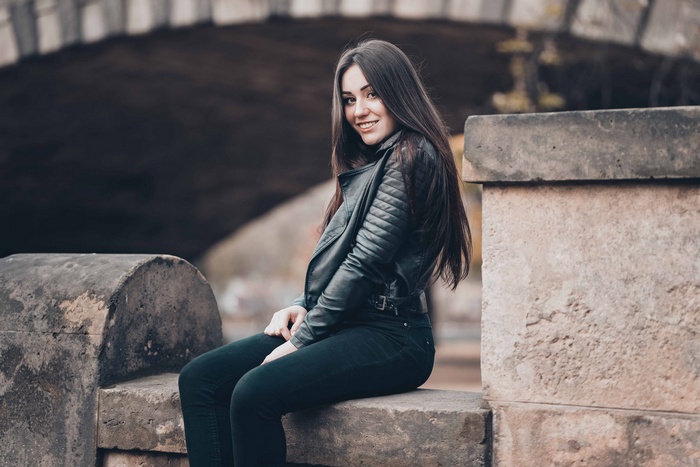 Woman in leather jacket sitting on stone ledge
